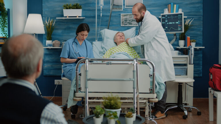 Doctor using stethoscope on ill senior woman in hospital bed